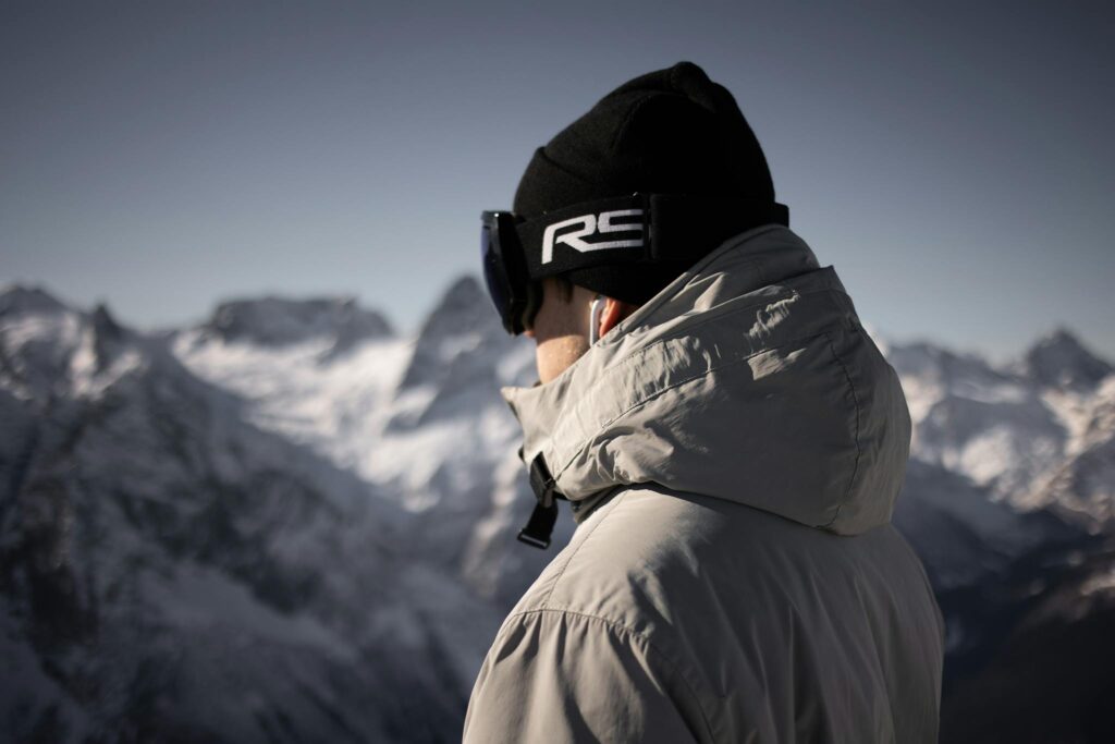Person in warm clothing enjoying a winter mountain view, featuring a beanie and goggles.
