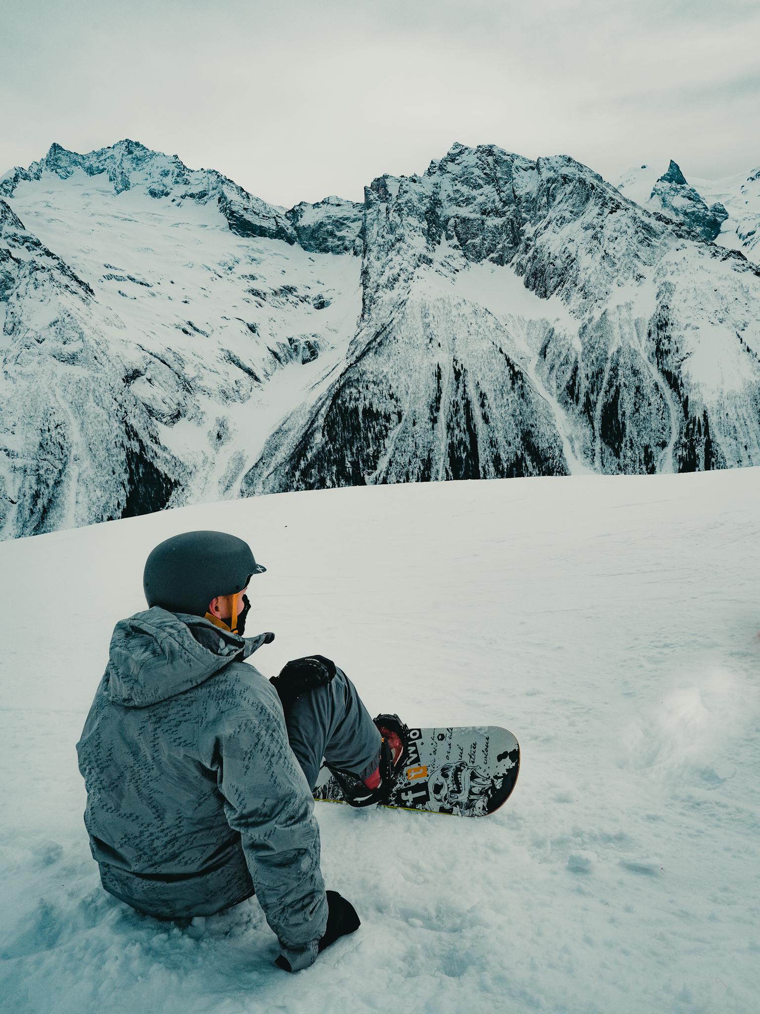 Snowboarder resting on snowy peak, surrounded by breathtaking mountain scenery.